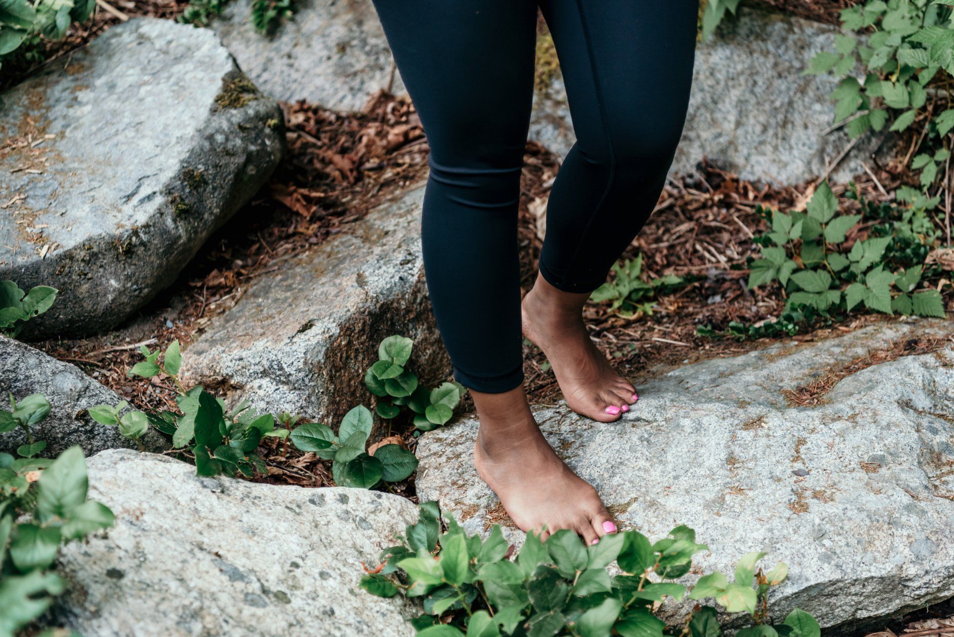 Blote voeten op rotsen, omringd door groene planten. Gekleed in zwarte leggings.