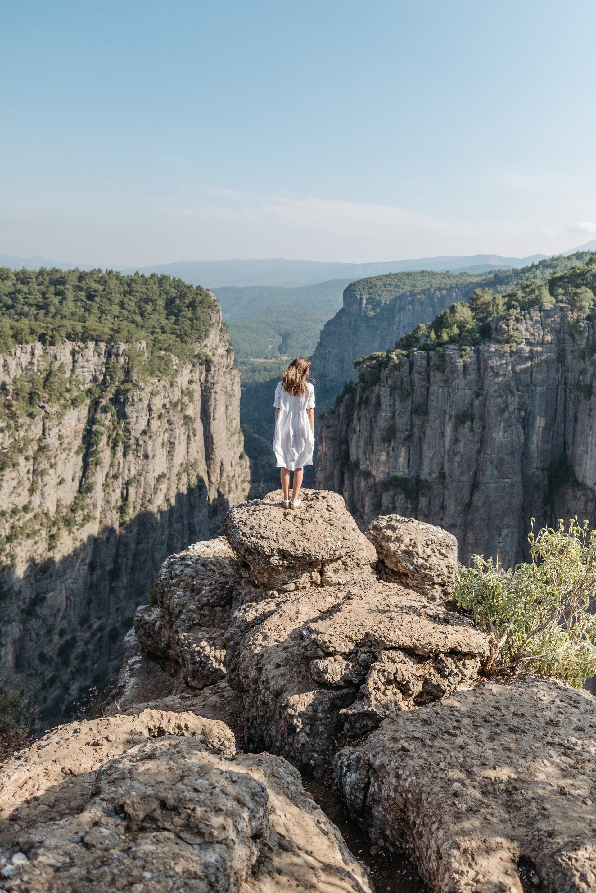 A woman is standing on top of a rocky cliff overlooking a canyon.