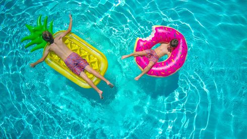 Two people relaxing on inflatable pool floats in clear blue water.