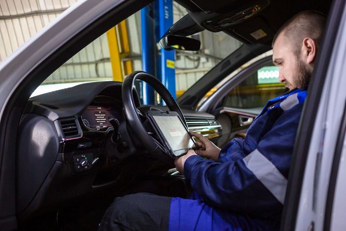 Mechanic in blue coveralls using a tablet inside a car during a vehicle inspection