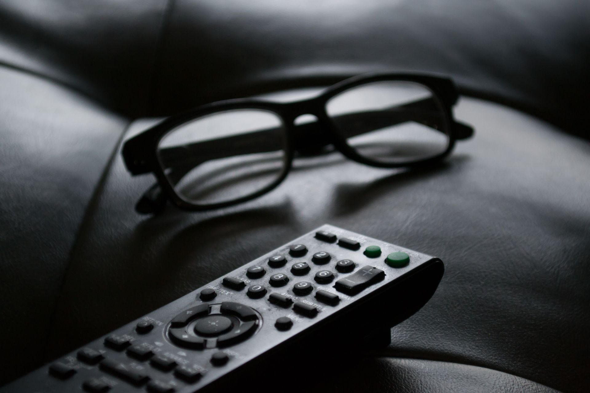 A pair of glasses sitting next to a remote control on a couch.