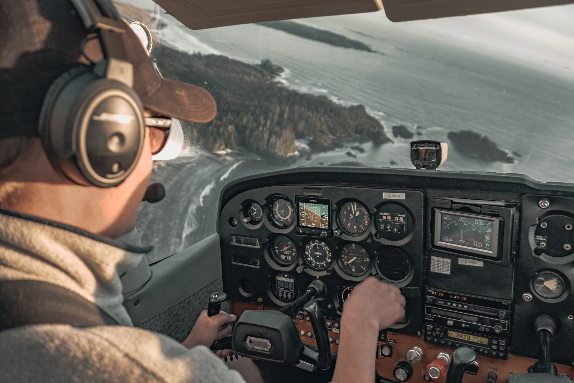 Pilot navigating small aircraft over rugged coastline while monitoring analog flight instruments.