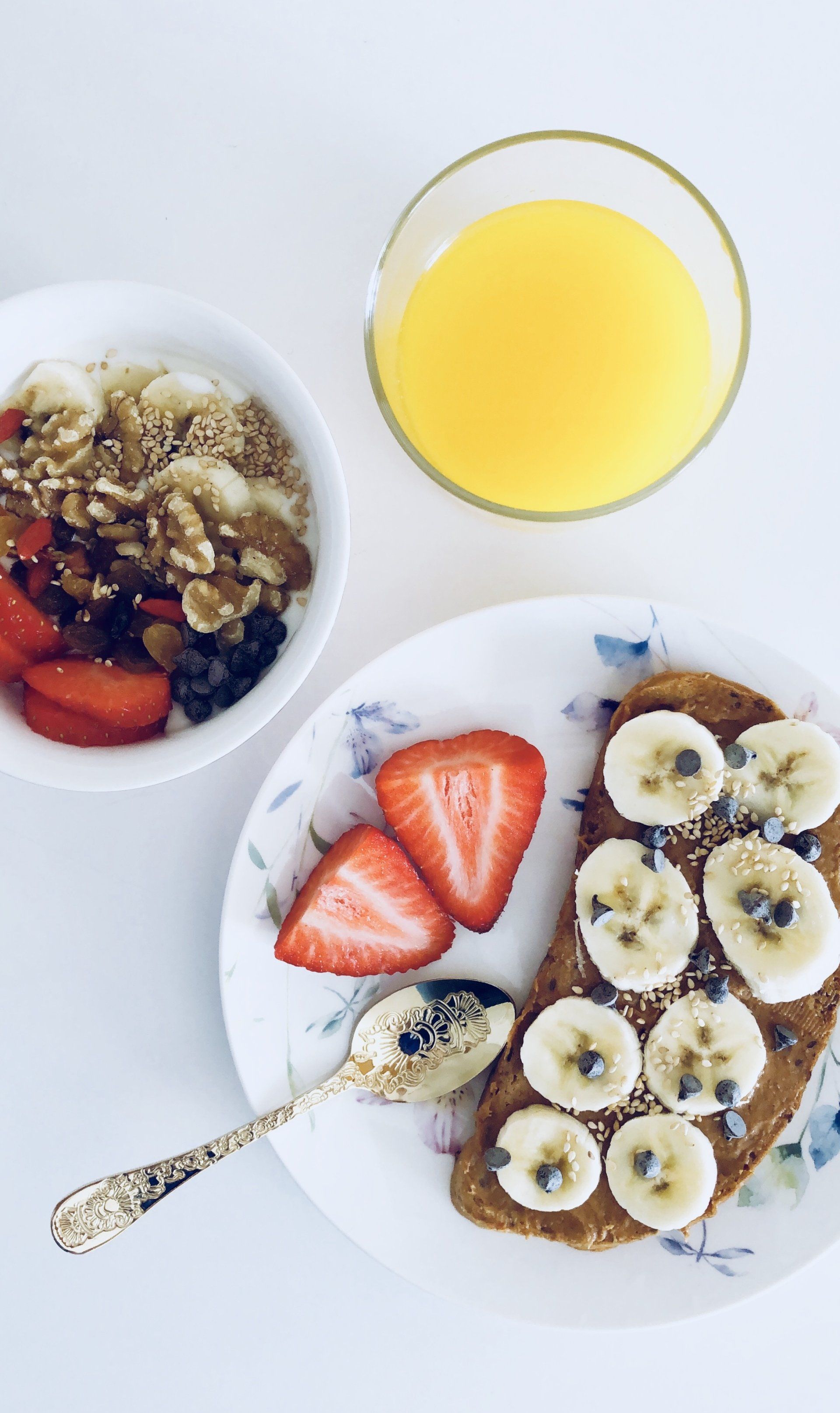 A plate of toast with bananas and strawberries next to a bowl of granola and a glass of orange juice.