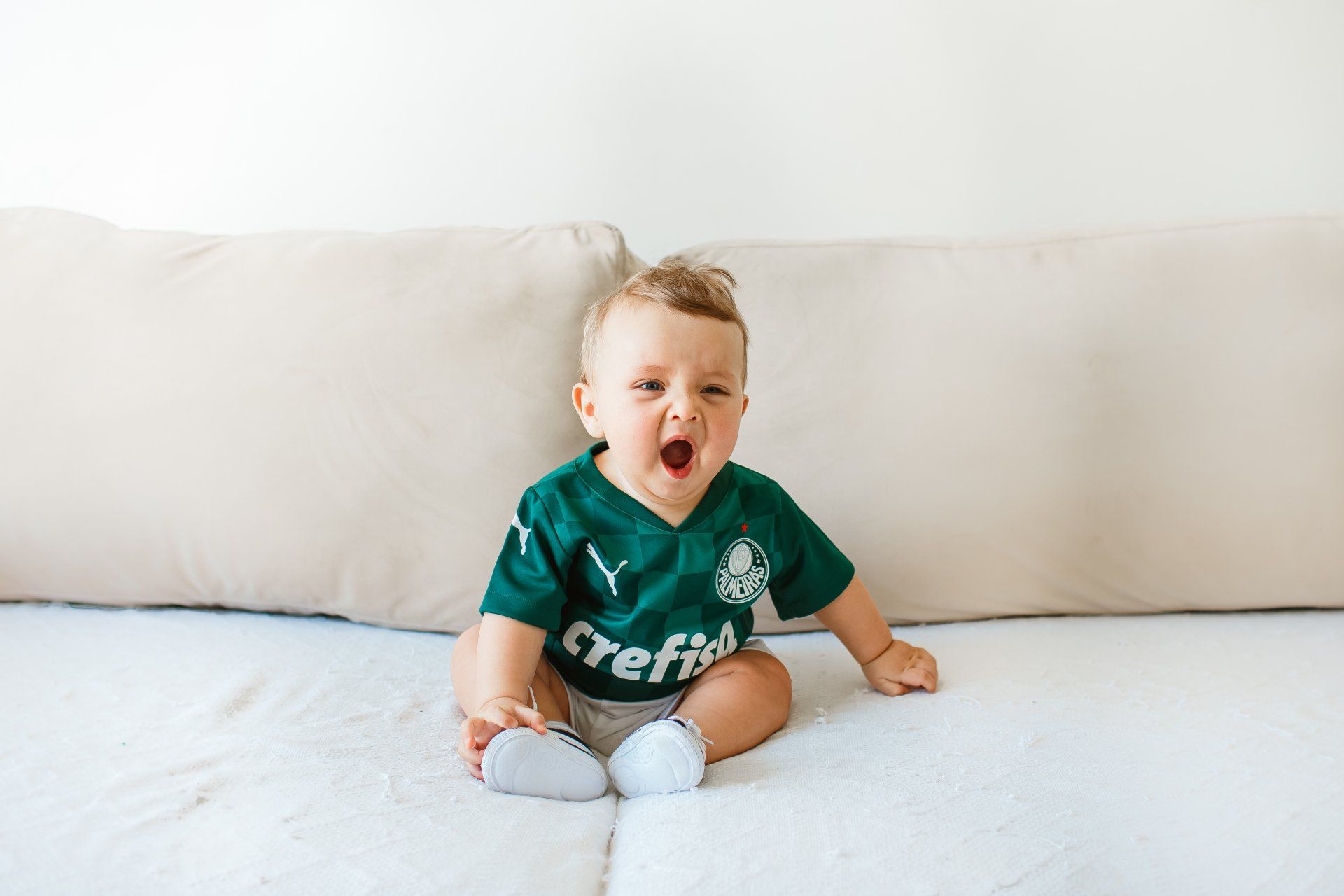 En baby sidder på en sofa iført en grøn skjorte.