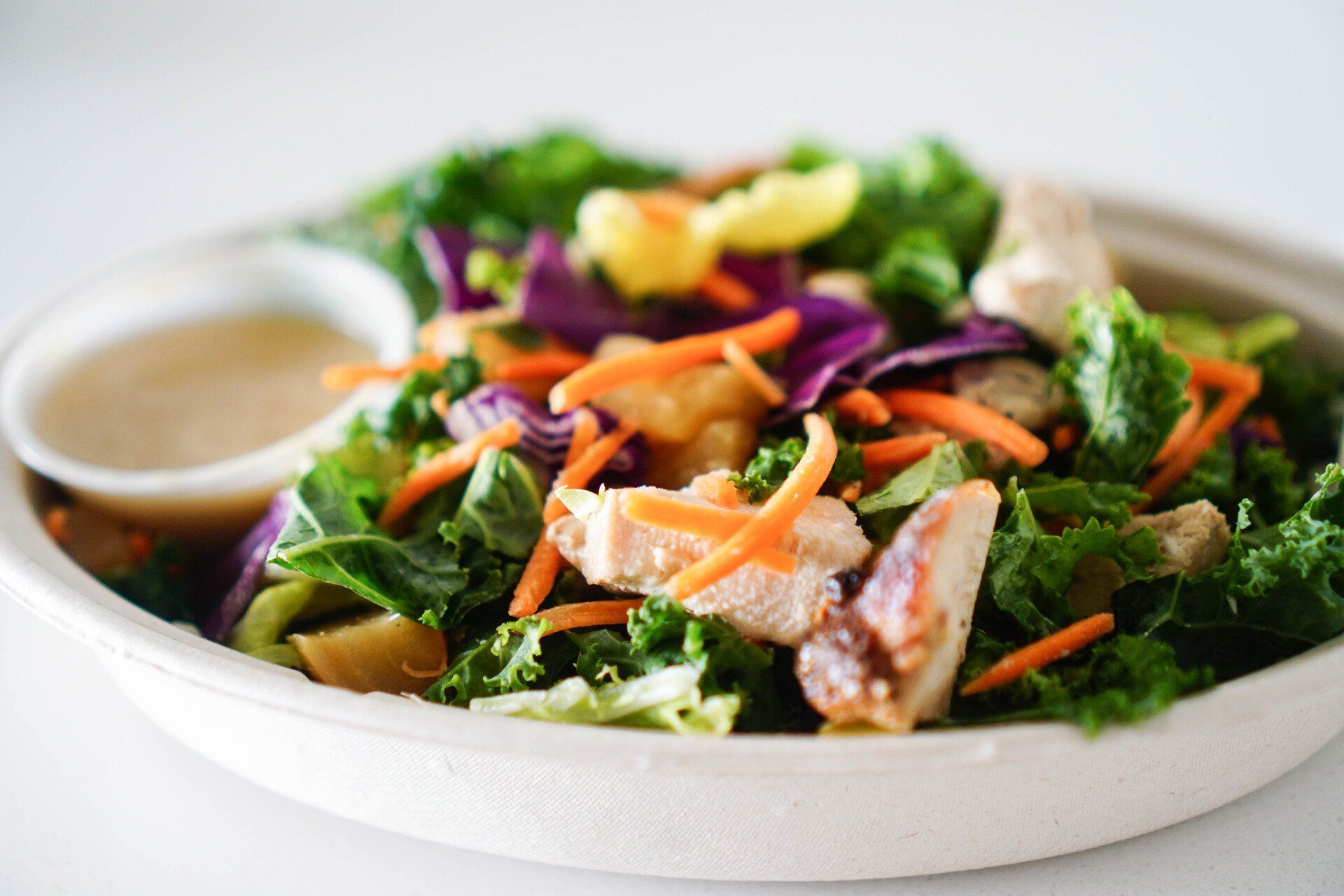 Een close-up van een salade met kip, wortelen, sla en een dipsaus op een bord.