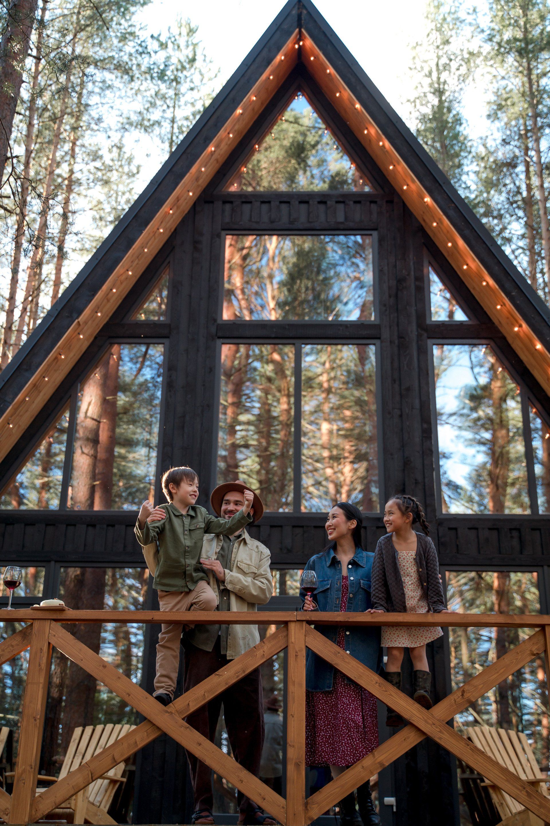 A family is standing on a balcony in front of a cabin in the woods.