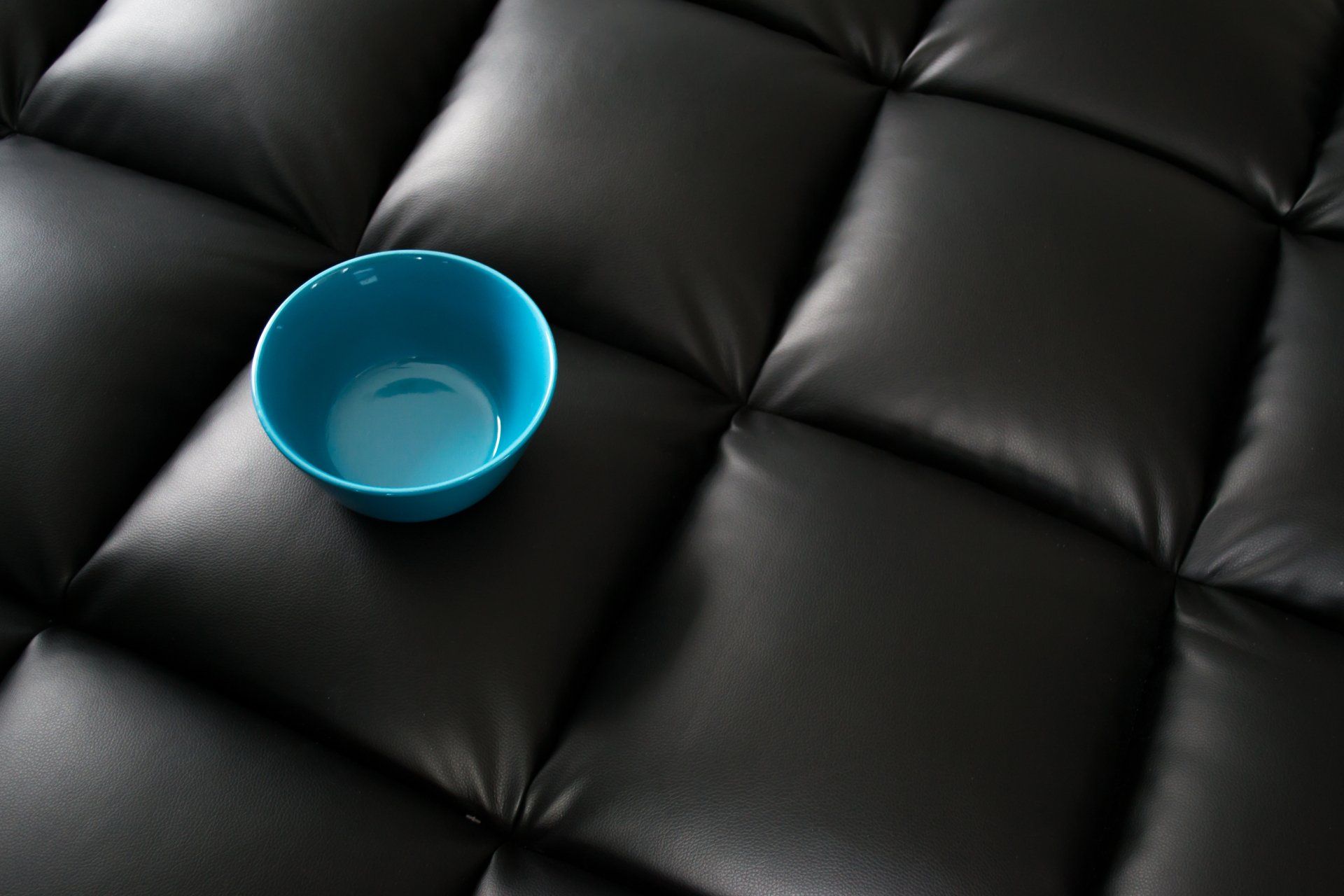 A blue bowl is sitting on a black leather couch.