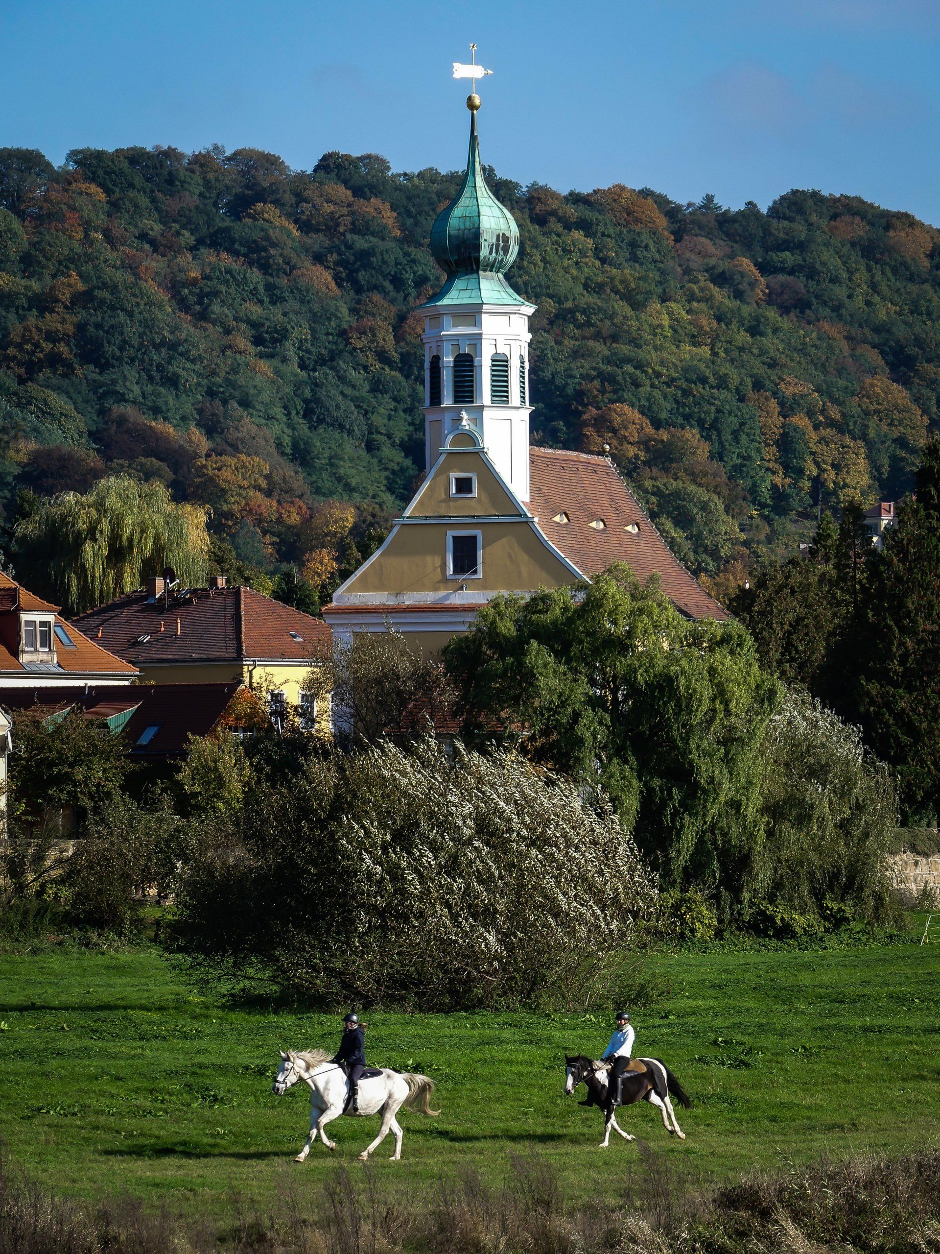 Zwei Menschen reiten auf einem Feld mit einer Kirche im Hintergrund