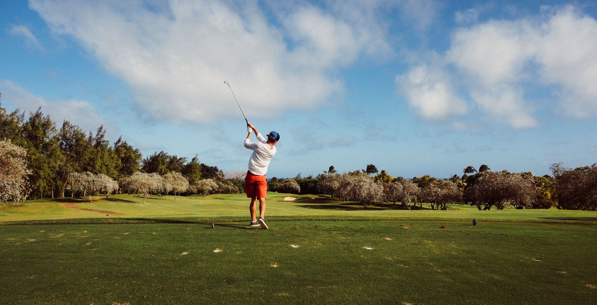 Man swinging golf club on a green, sunny day.