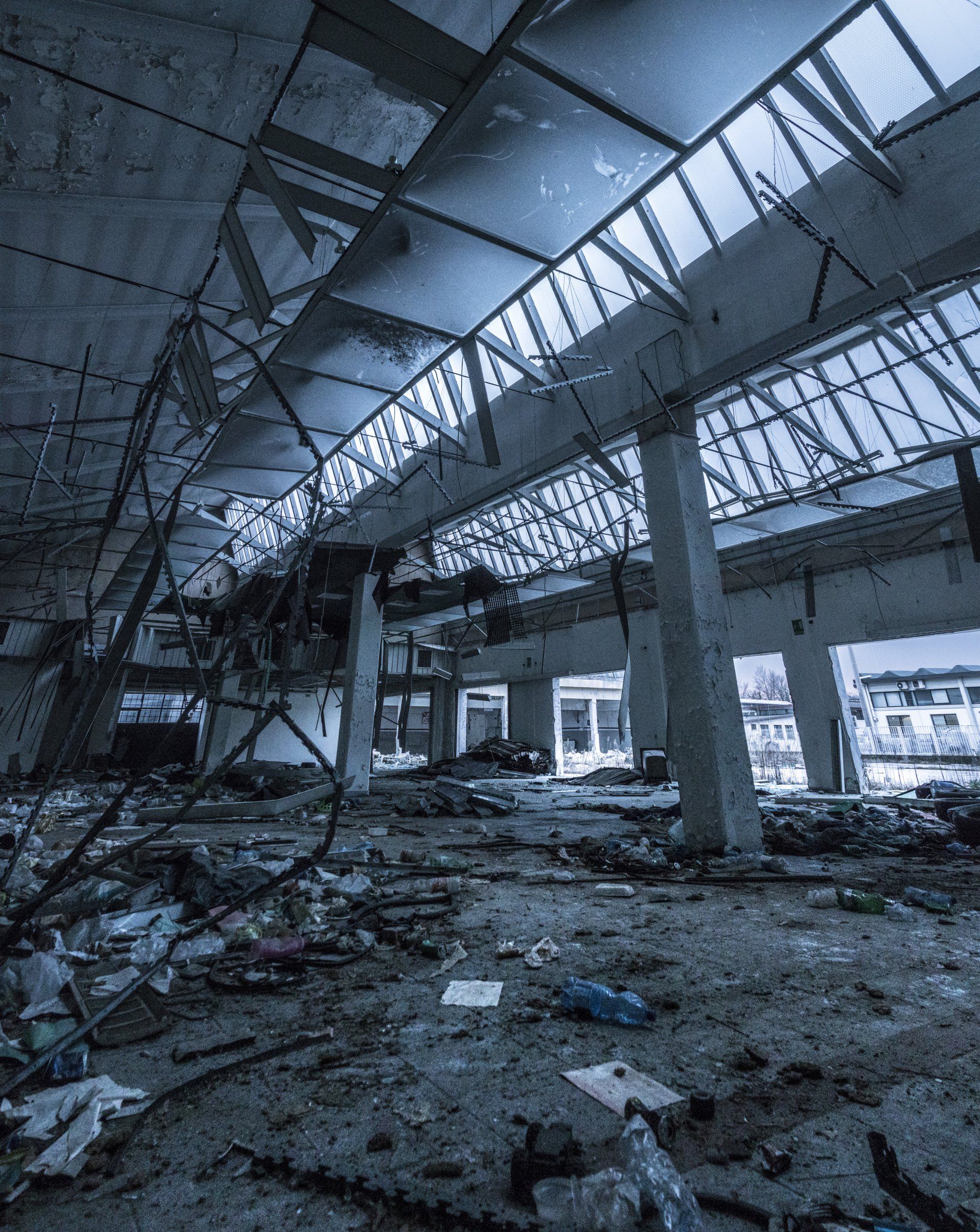 Interior of a damaged building, rubble on the floor, sections of the ceiling collapsed, pale blue lighting.