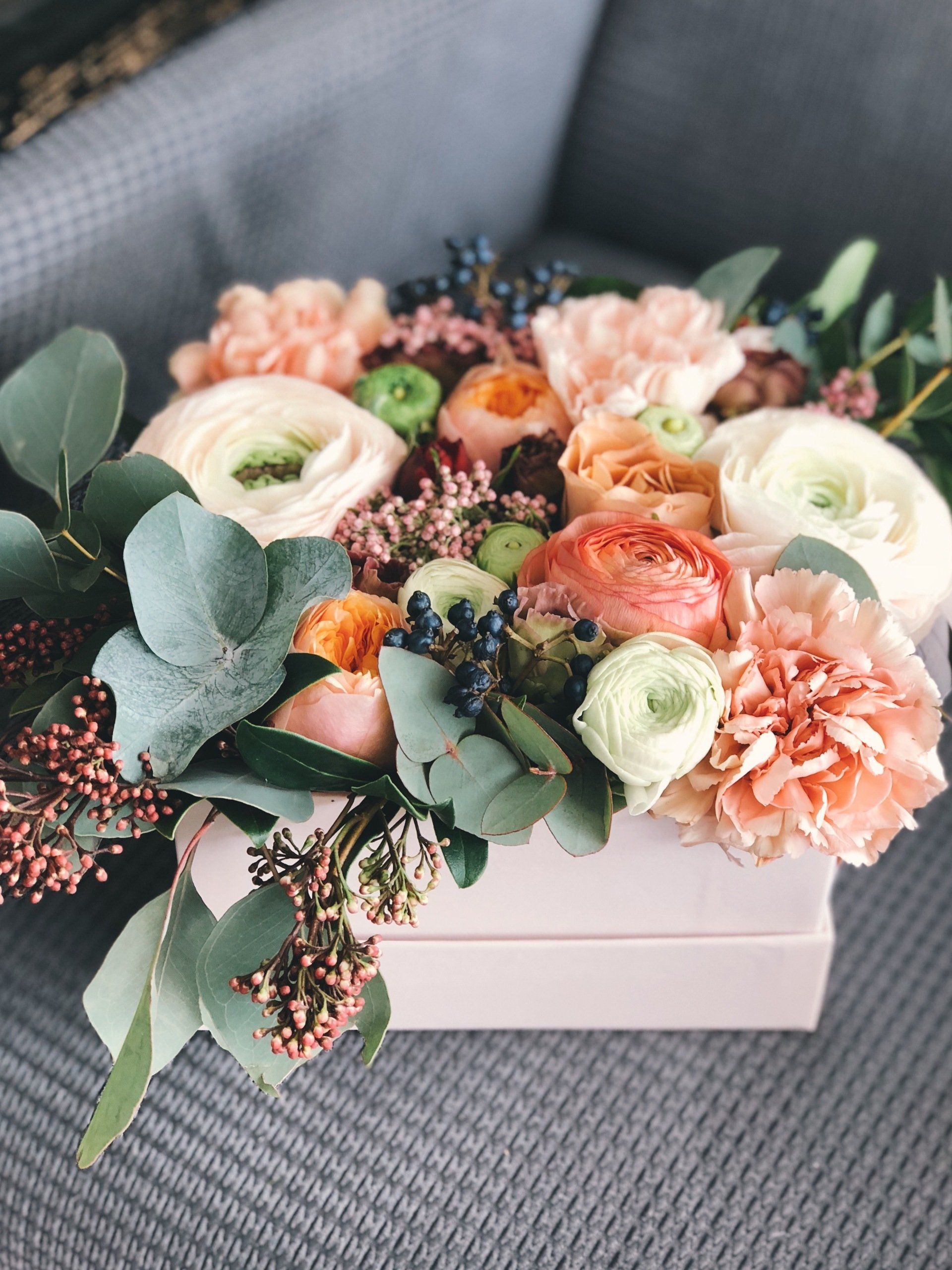 A box filled with flowers is sitting on a couch.