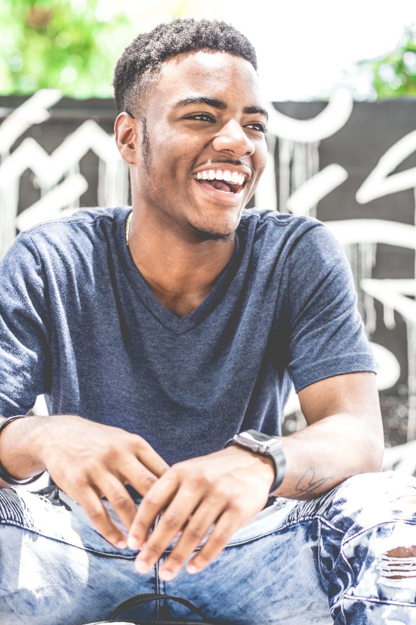 Smiling man in a blue T-shirt sitting outdoors against a graffiti wall