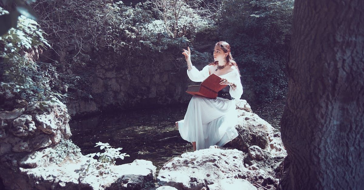 A woman in a white dress is standing on a rock in the woods.