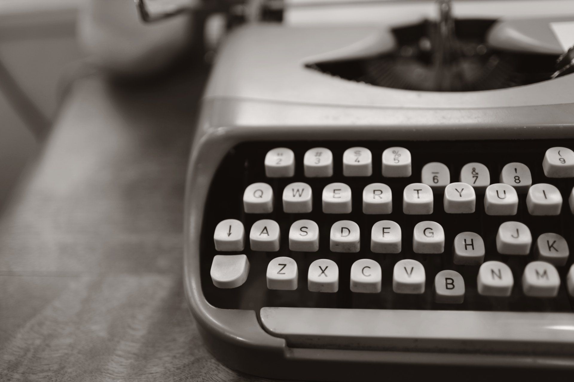 Close-up of a vintage typewriter with round keys on a desk, in black and white.