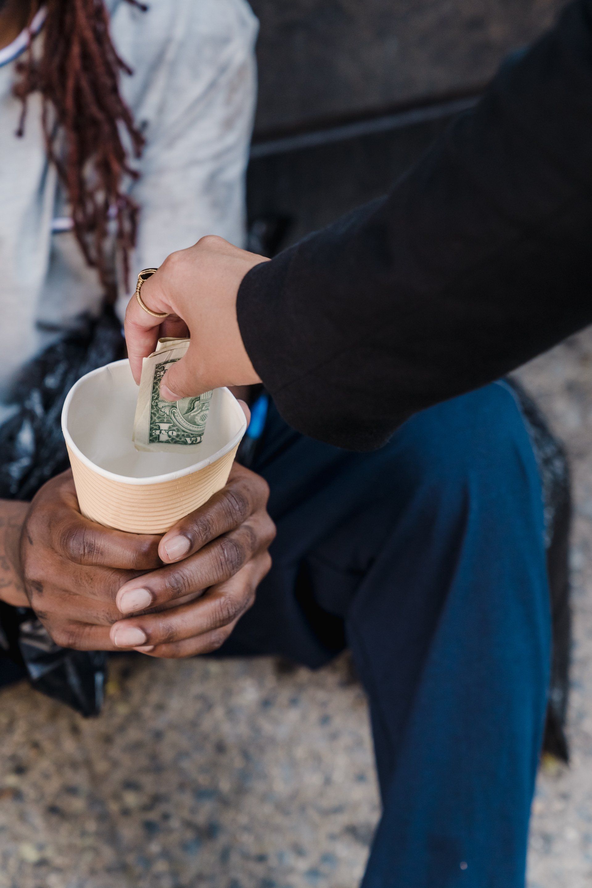 A person placing a dollar bill into a paper cup held by another individual. Chet's Roof charity and community service seattle