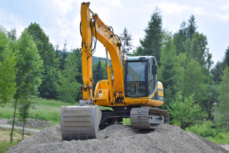 Yellow excavator on a pile of gravel, with a forest in the background.