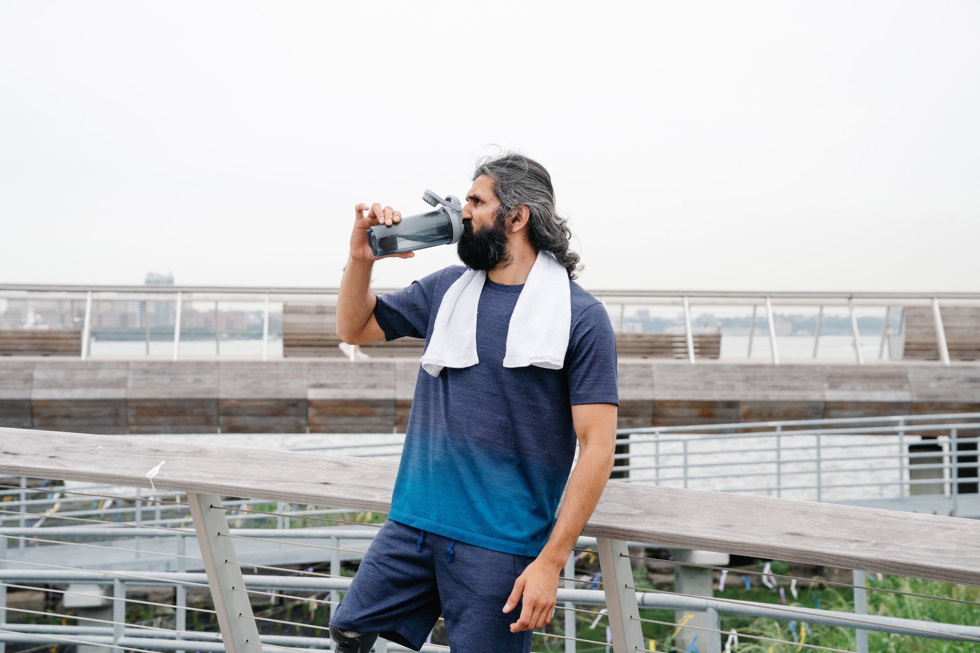 Een man met een handdoek om zijn nek drinkt water uit een fles.