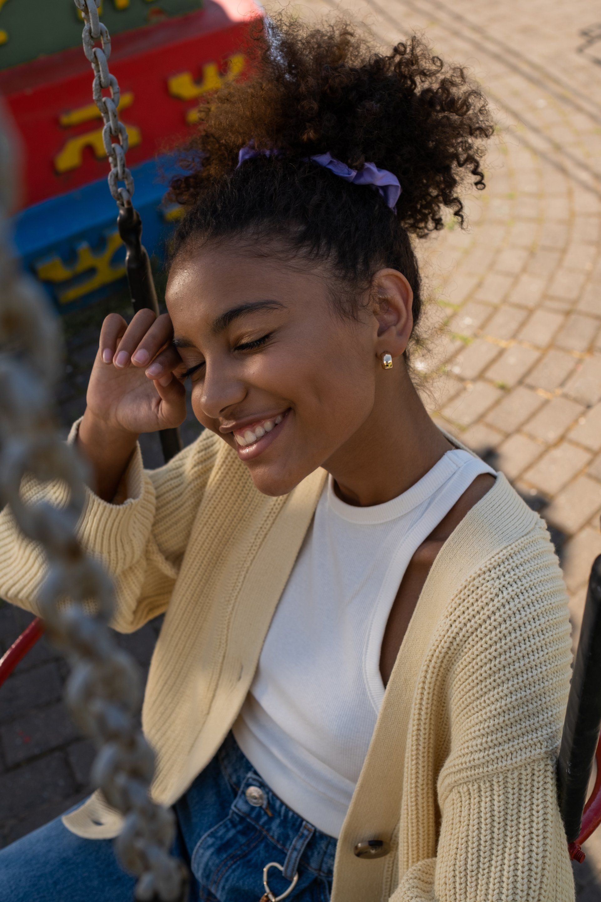 Smiling woman sitting outdoors, wearing a cream cardigan and white top, with a purple hair tie.