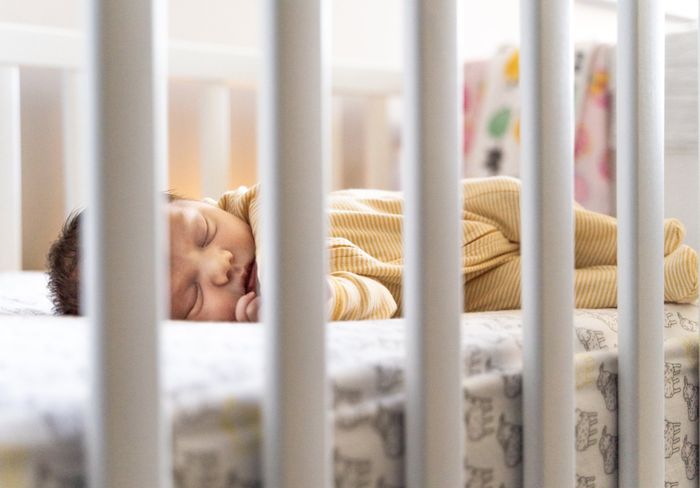 A baby is sleeping in a crib while her mother is having a restful postpartum.