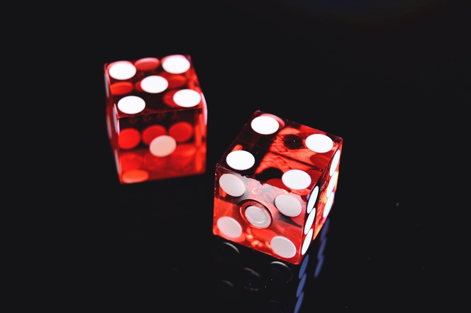 Two red dice with white dots on a black surface.