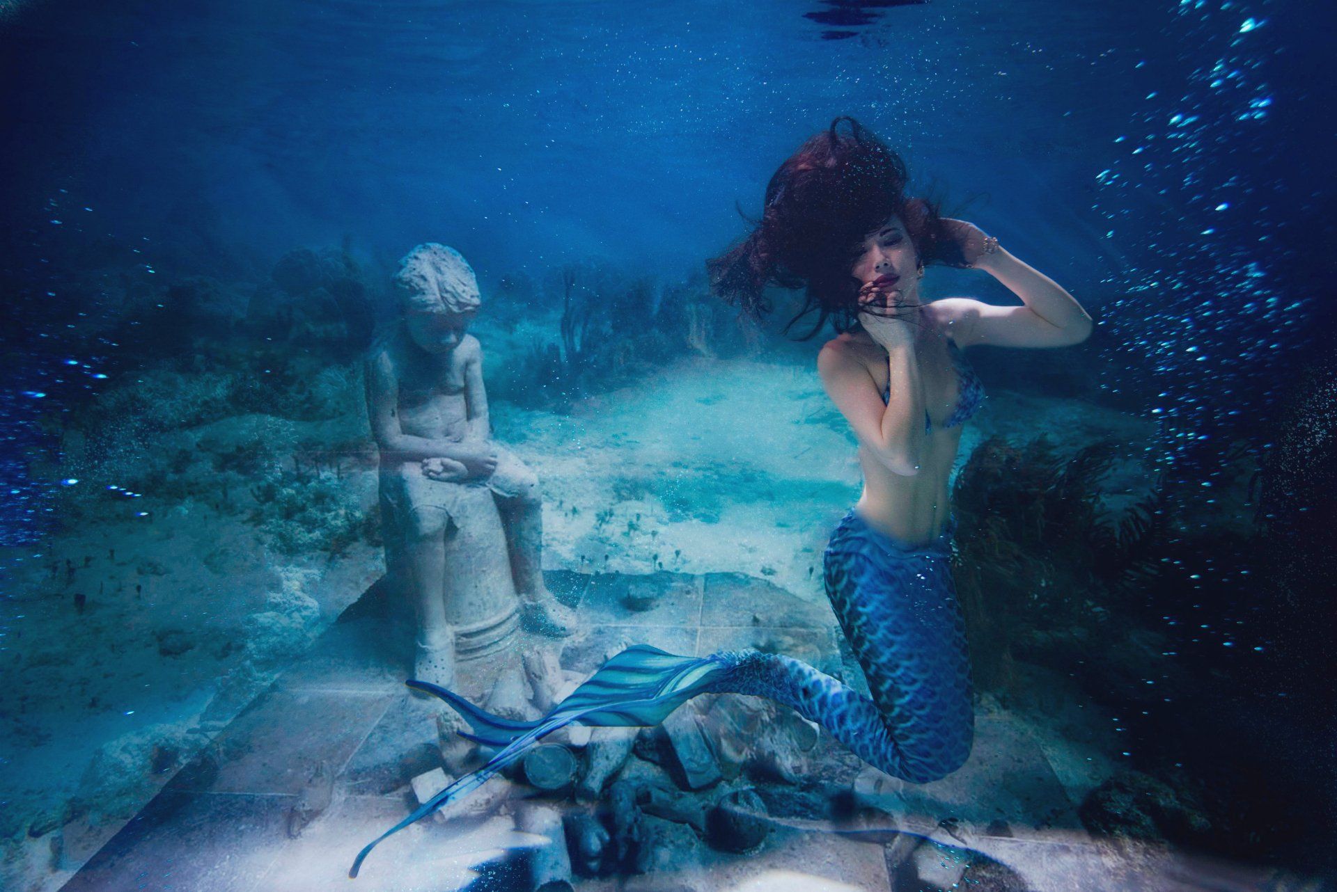 A woman dressed as a mermaid is swimming underwater in the ocean.