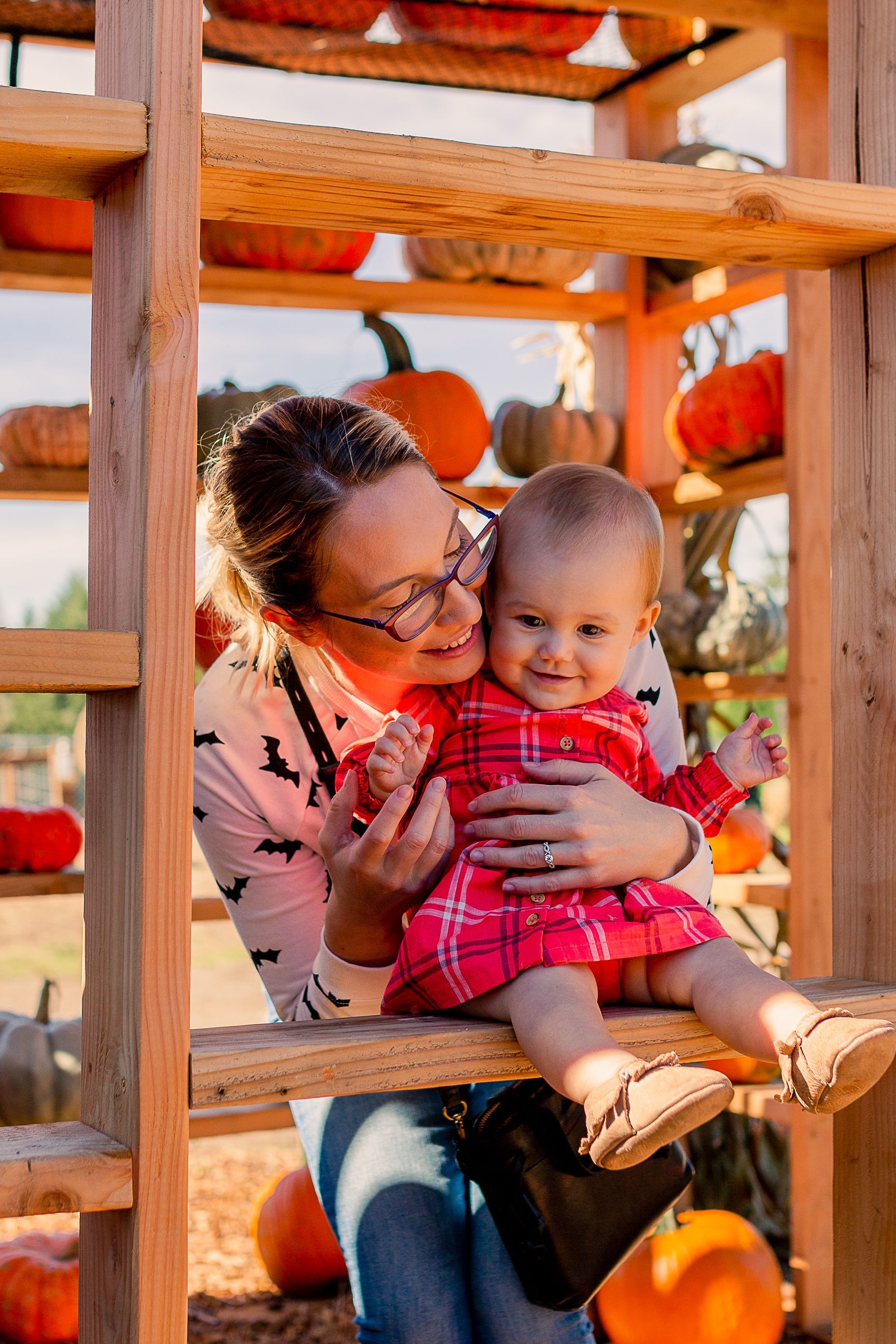 A woman is holding a baby on a wooden ladder at a pumpkin patch.