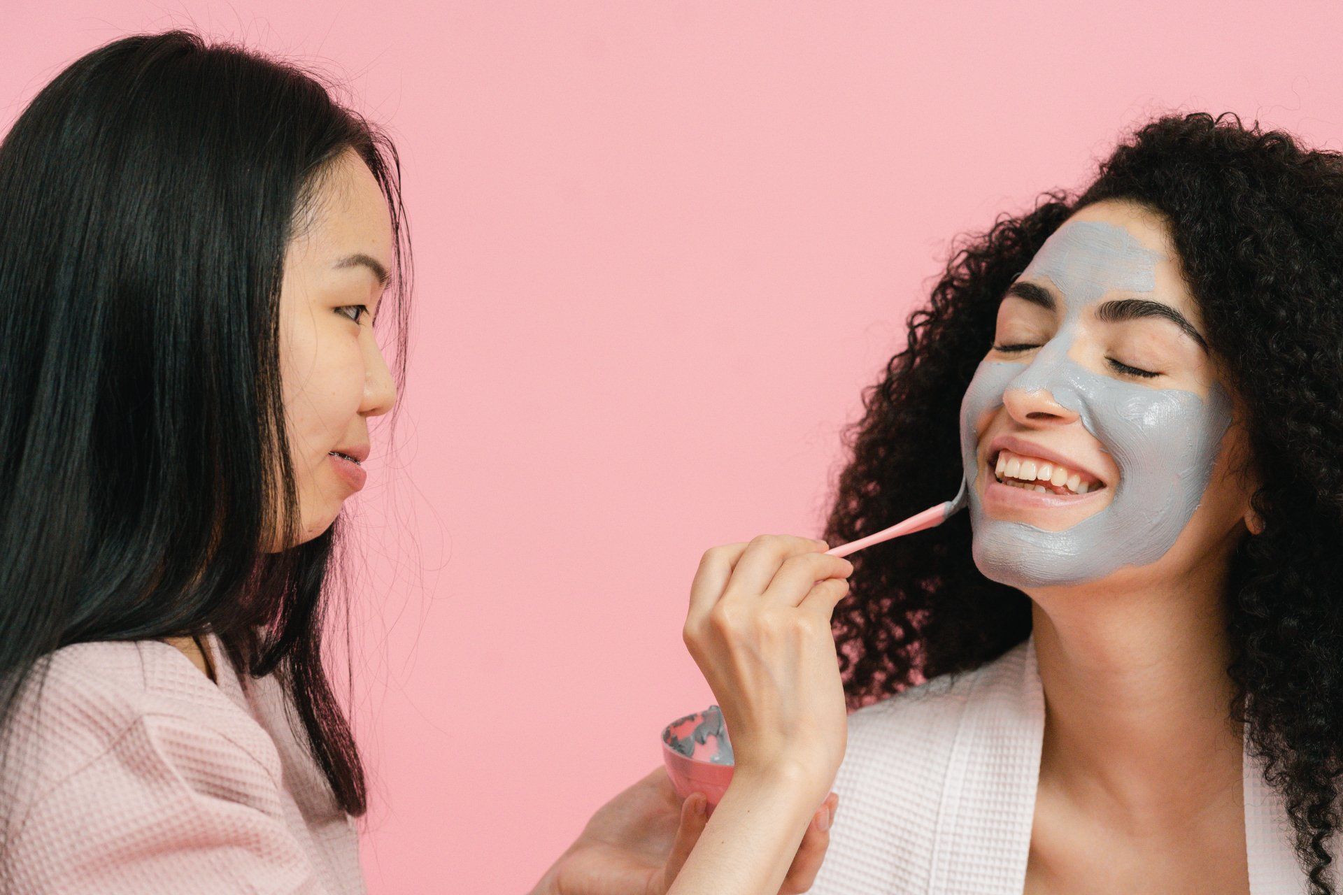 A woman is applying a clay mask to another woman 's face.