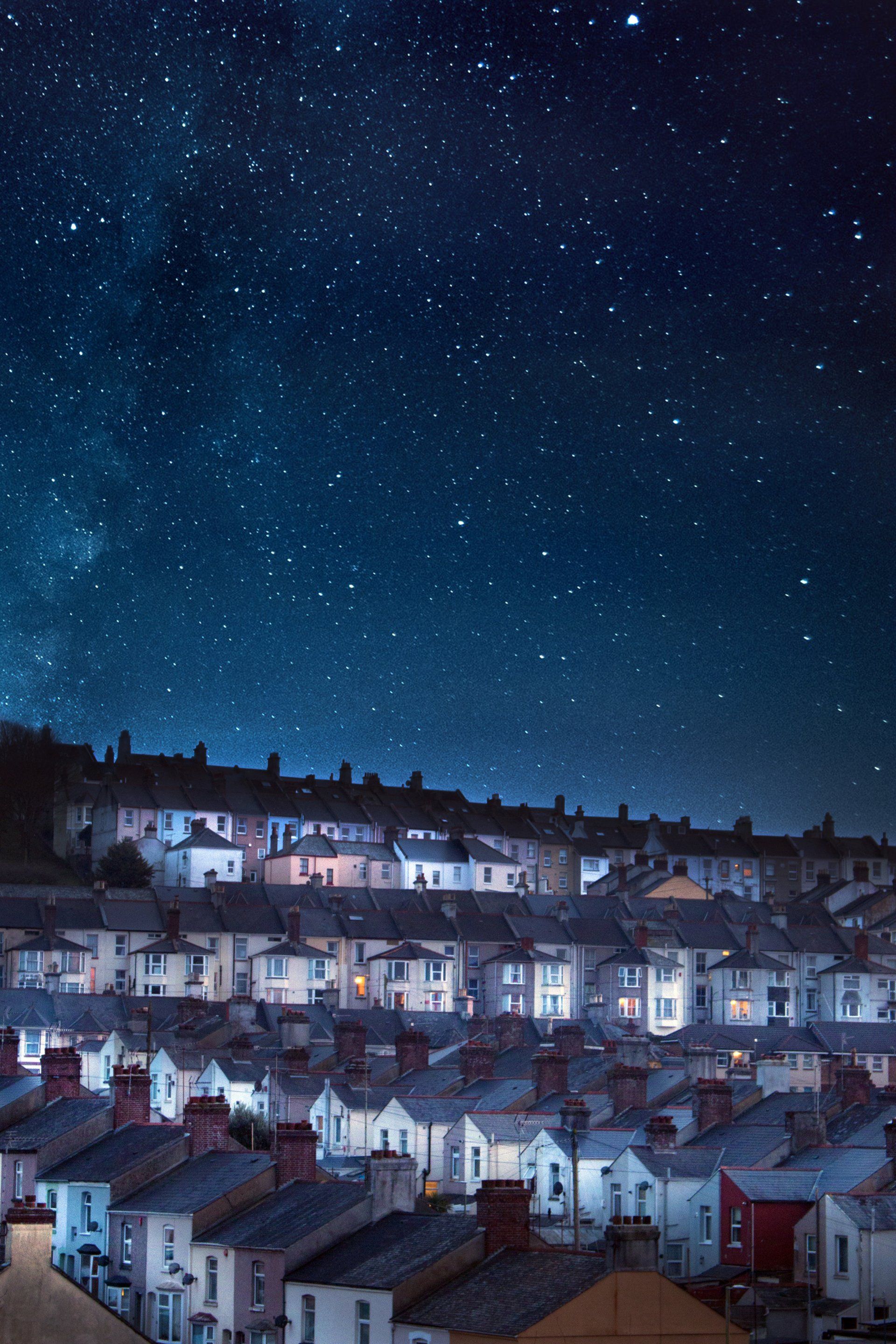Starry night sky over rows of lit houses in a town