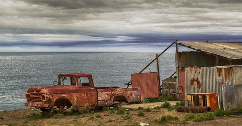 An old rusty truck is parked on the shore of a body of water