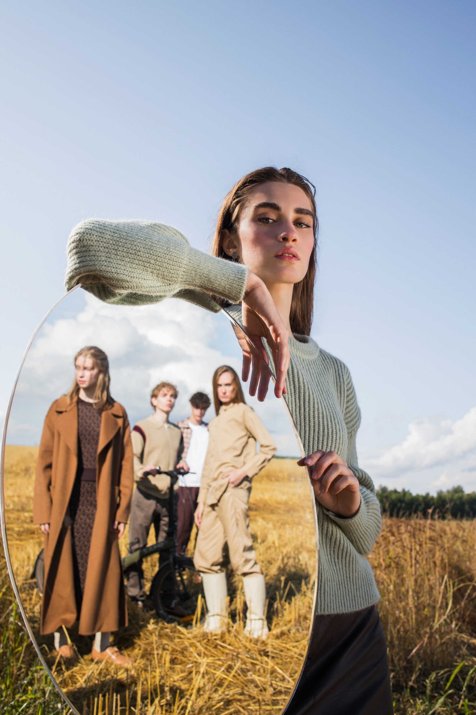A woman is holding a mirror in front of a group of people in a field.