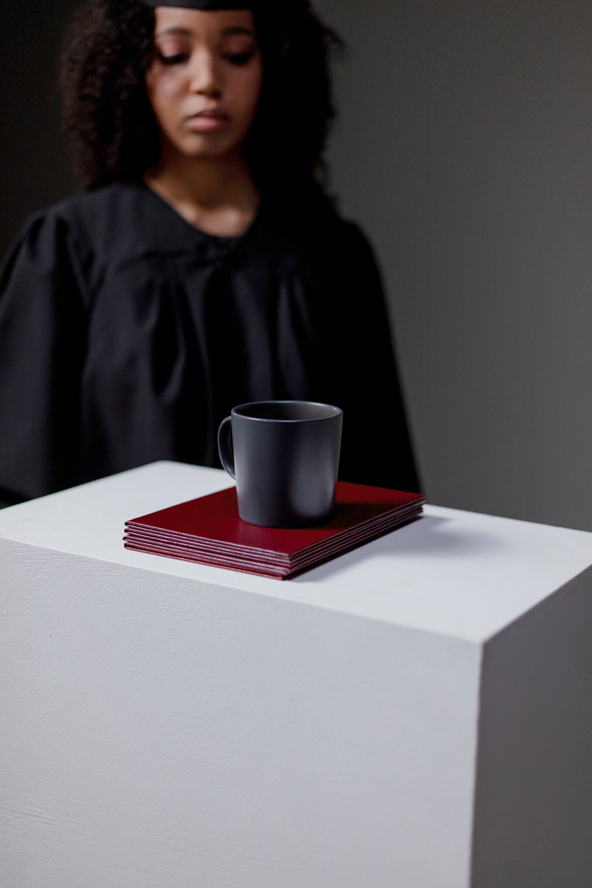 A woman in a graduation cap and gown is standing behind a table with a cup on it