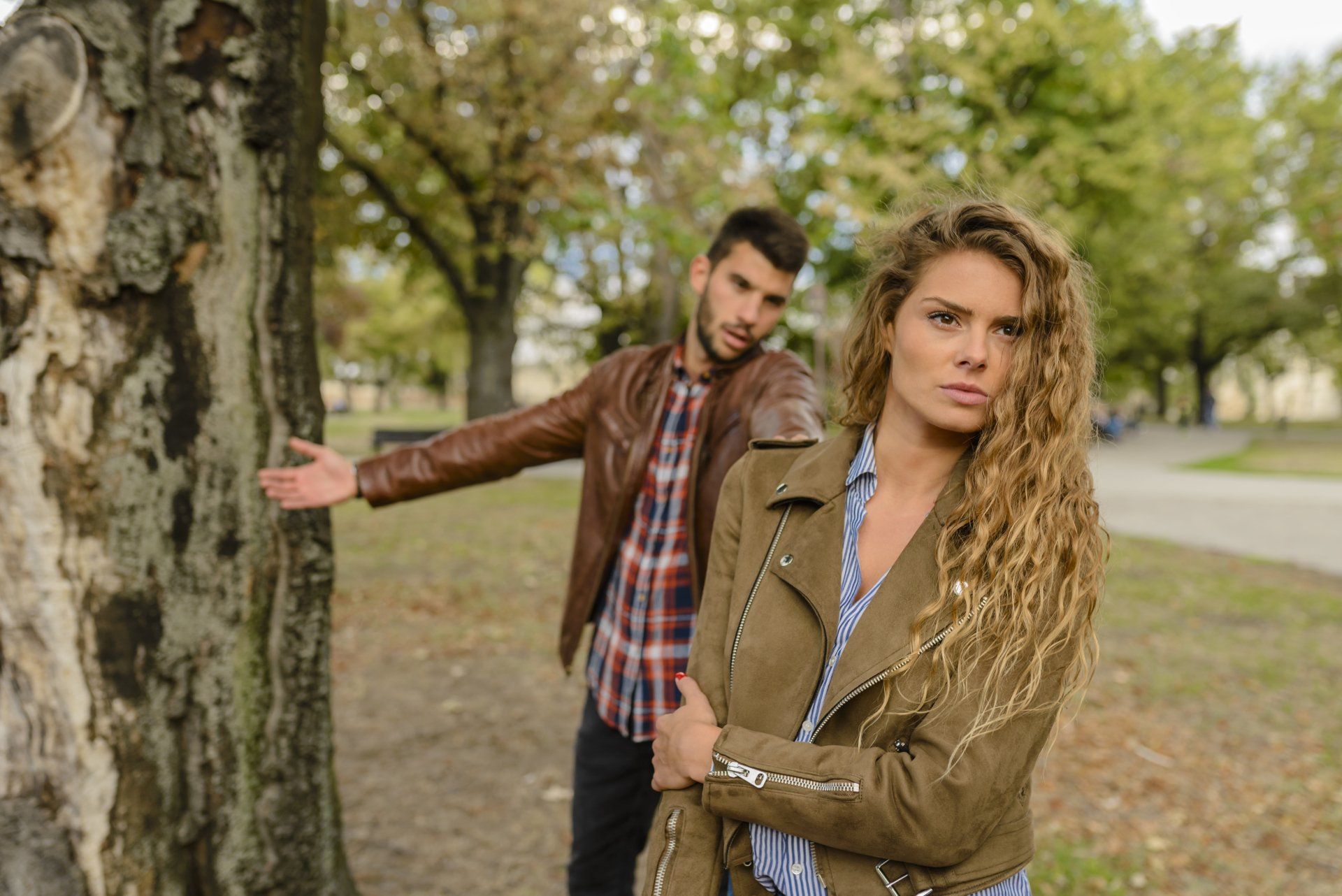 A man and a woman are standing next to a tree in a park.