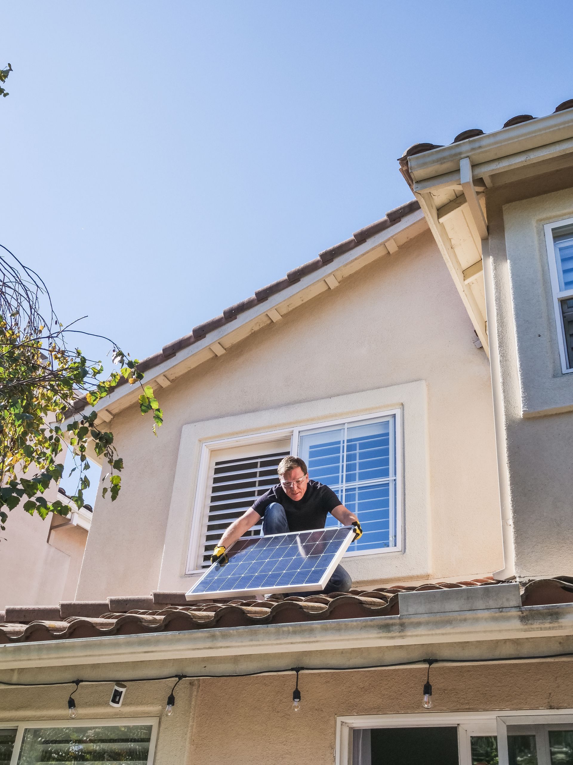 Person on a roof installing a solar panel on a beige house under a blue sky