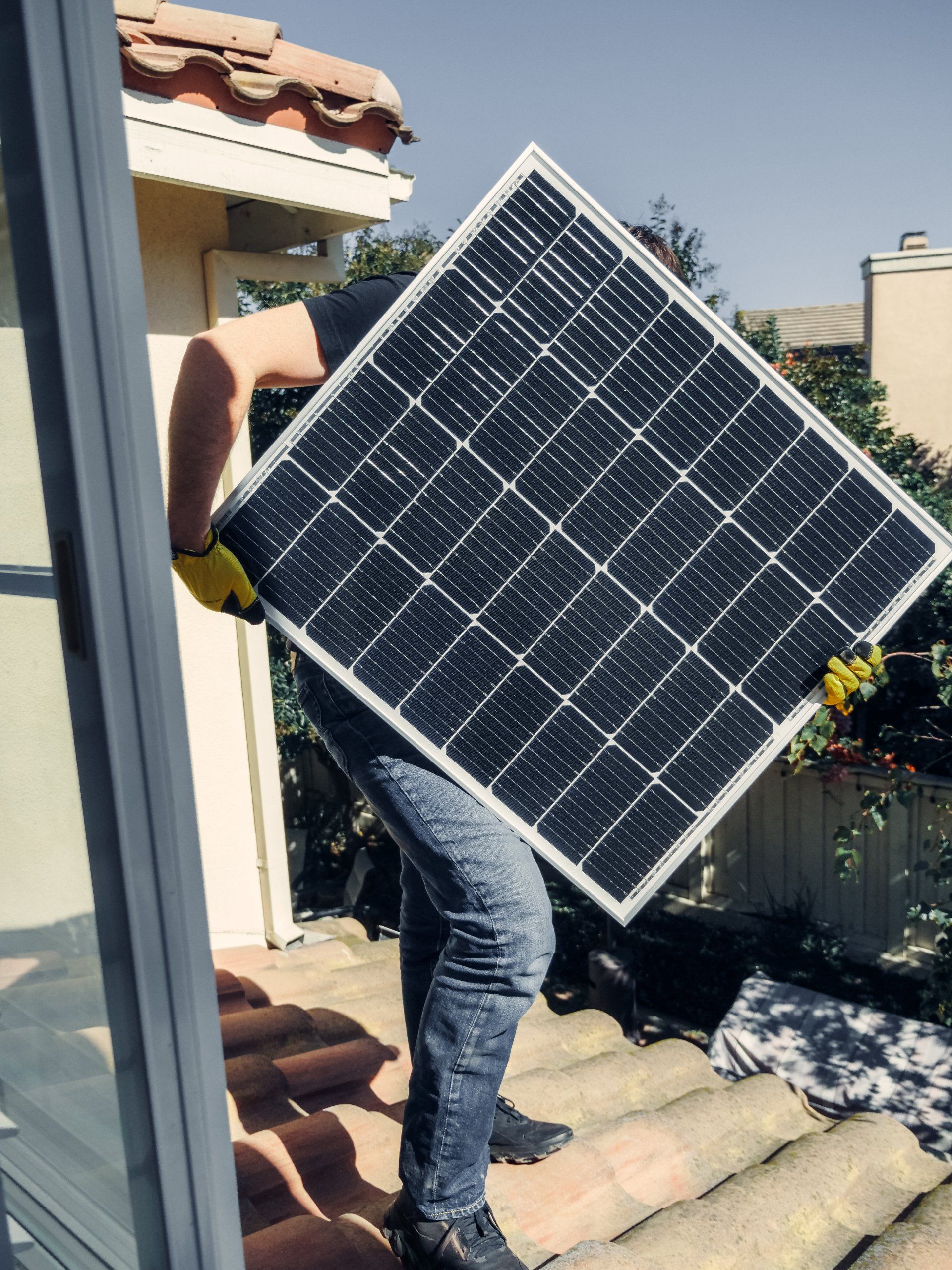 Person carrying a large solar panel up outdoor steps near a house