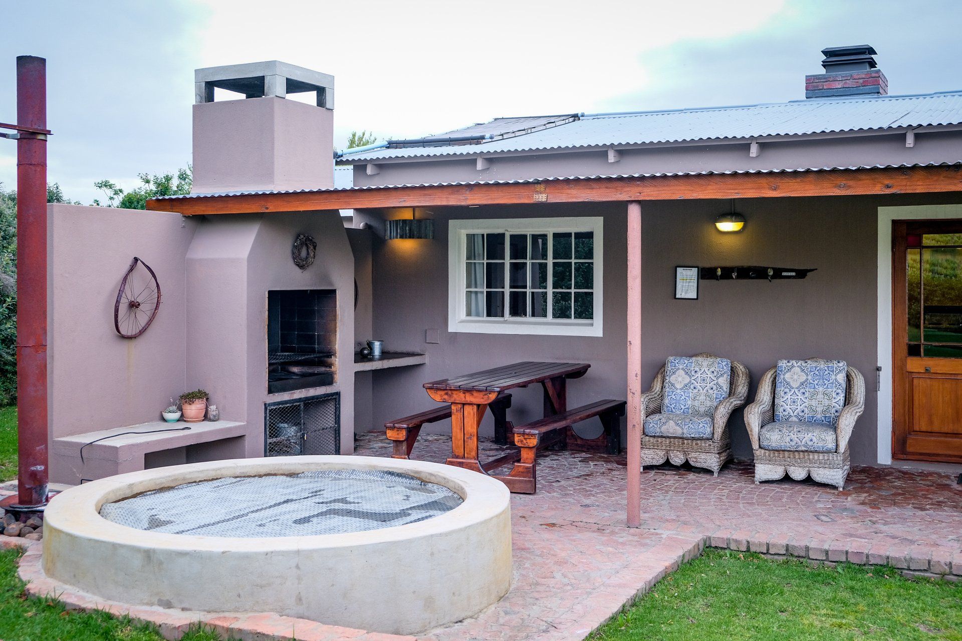 Patio with a round hot tub, outdoor fireplace, covered seating, and two chairs beside a house