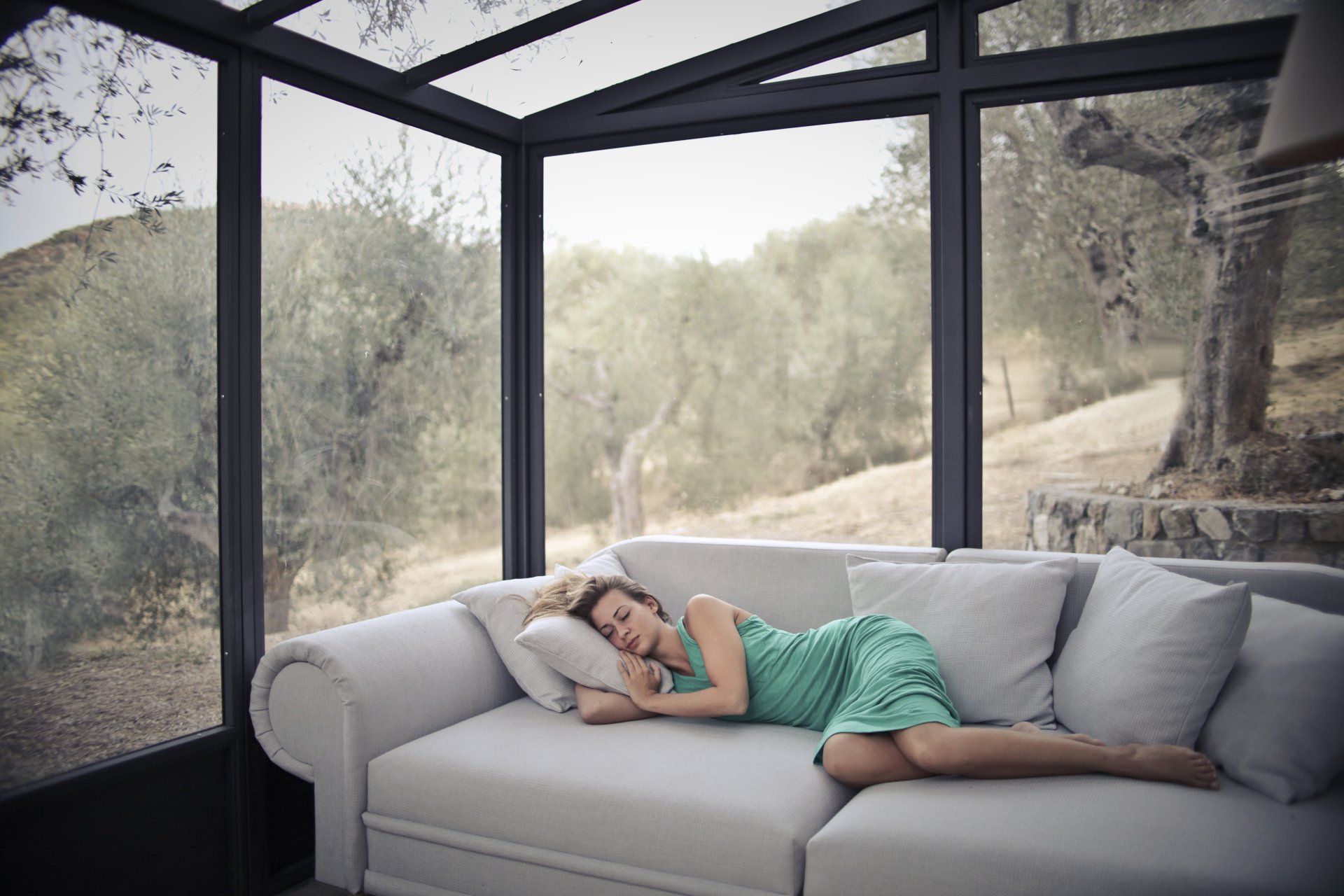 A woman is sleeping on a couch in a conservatory.