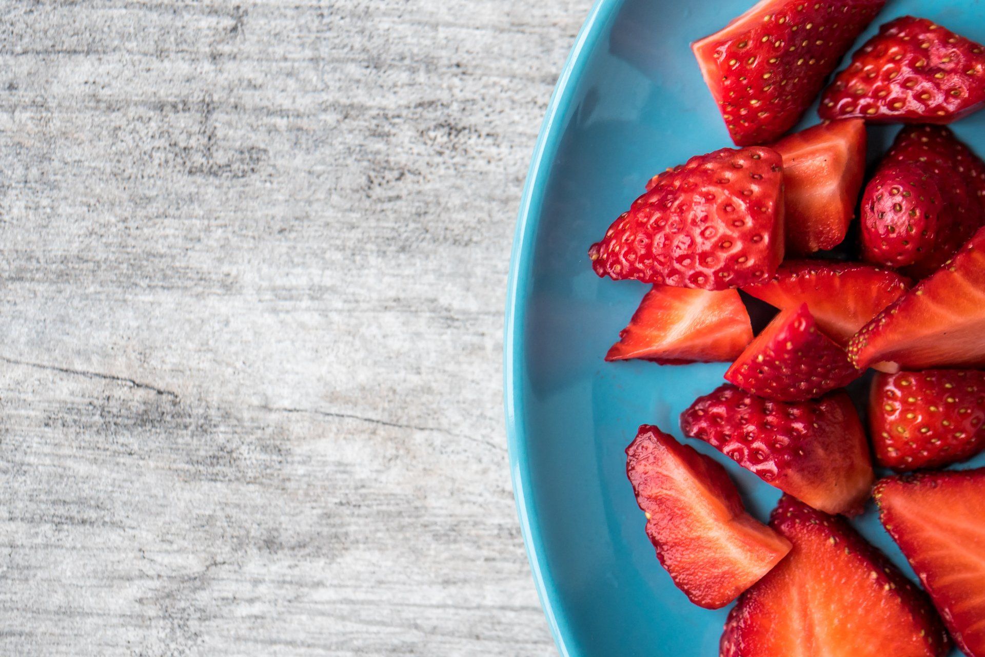 Blue plate with sliced strawberries on a light gray wooden surface.