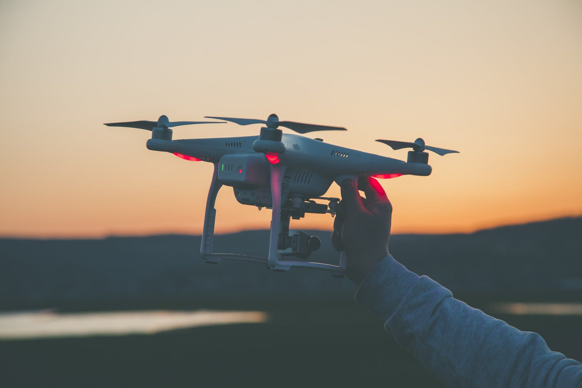 a person is holding a drone in their hand at sunset .
