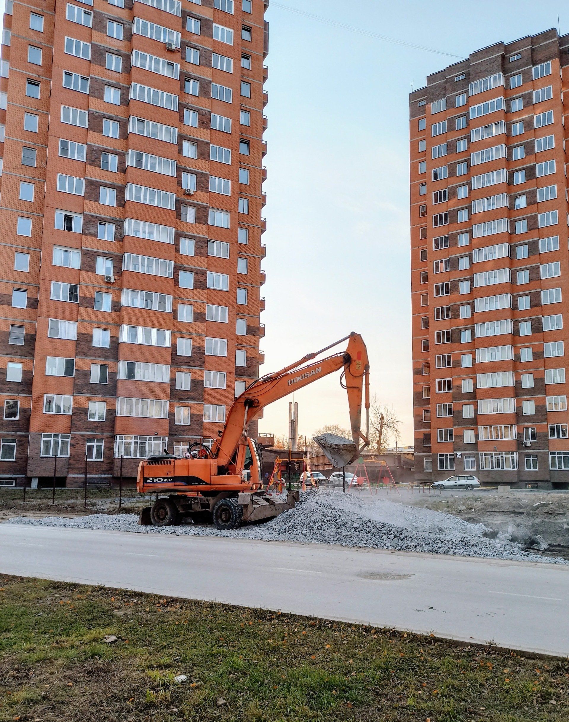 Orange excavator demolishing a building between two tall brick apartment towers