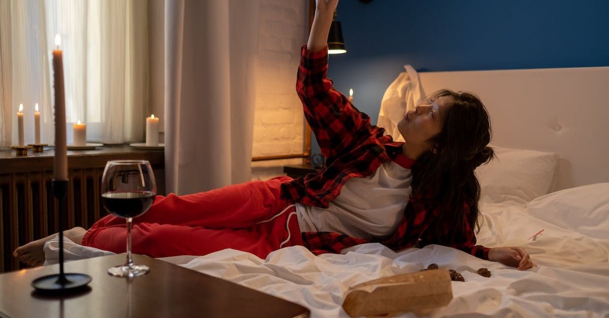 A woman is laying on a bed with a glass of wine and a candle.