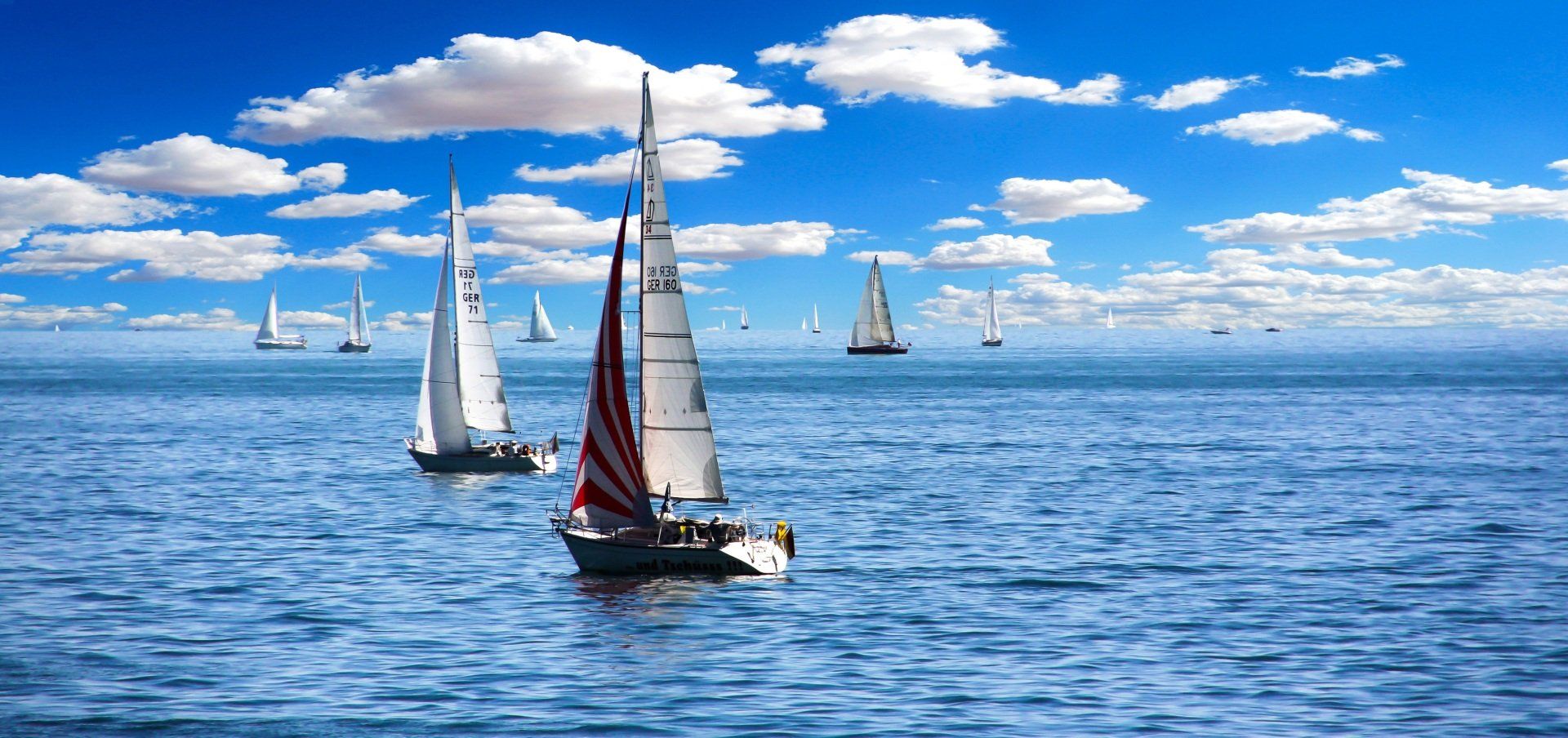 Sailboats on blue water under a bright blue sky with puffy white clouds.
