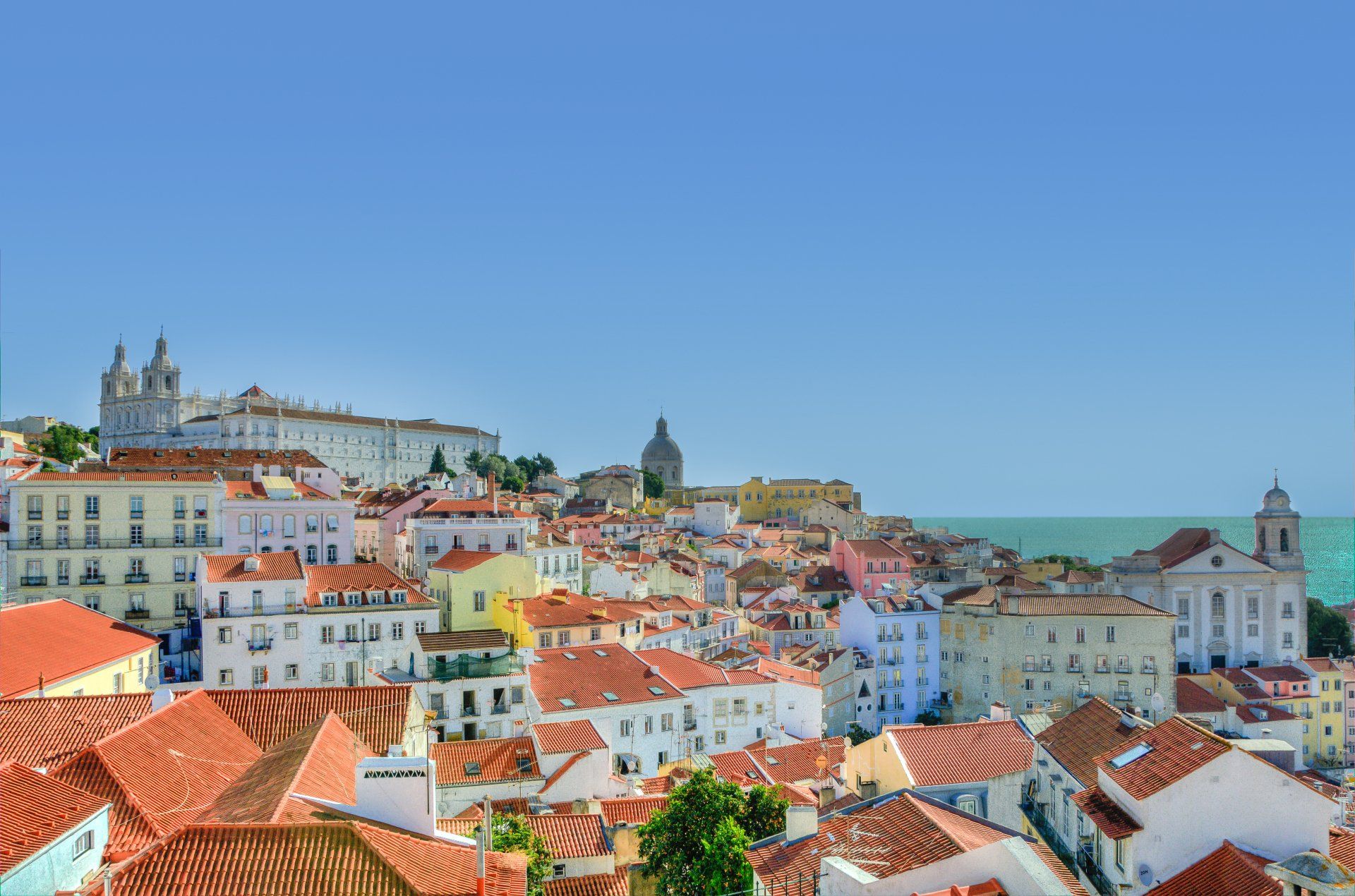 Uma vista aérea de uma cidade com telhados vermelhos e o oceano ao fundo.