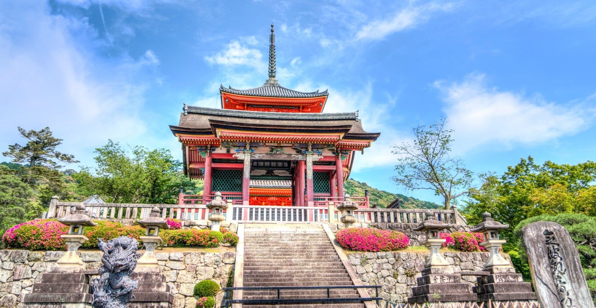 A temple with stairs leading up to it is surrounded by trees and flowers.
