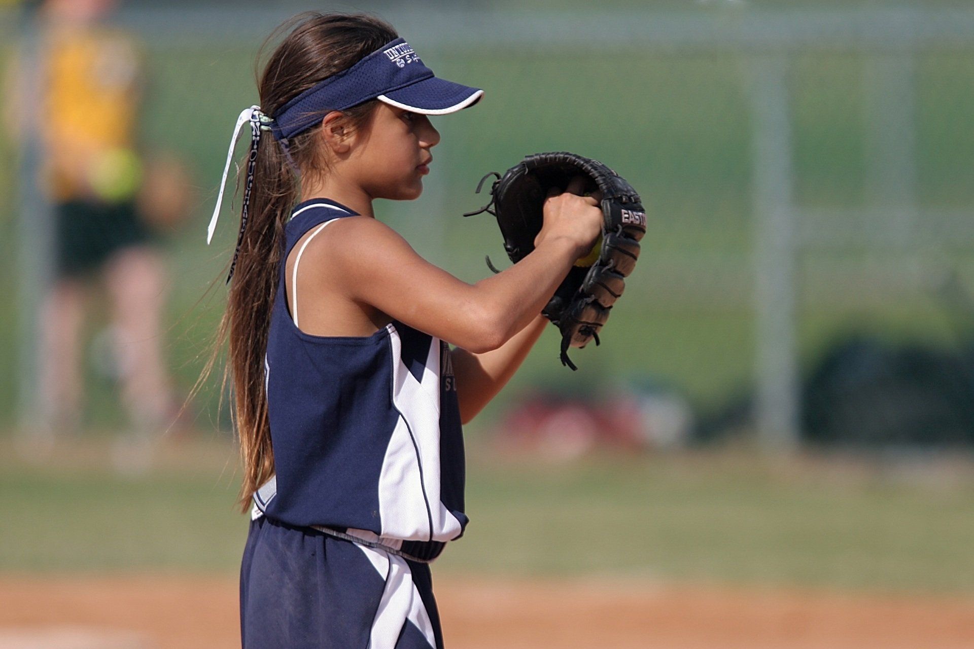 Girl in a blue softball uniform and visor prepares to pitch, holding a mitt.