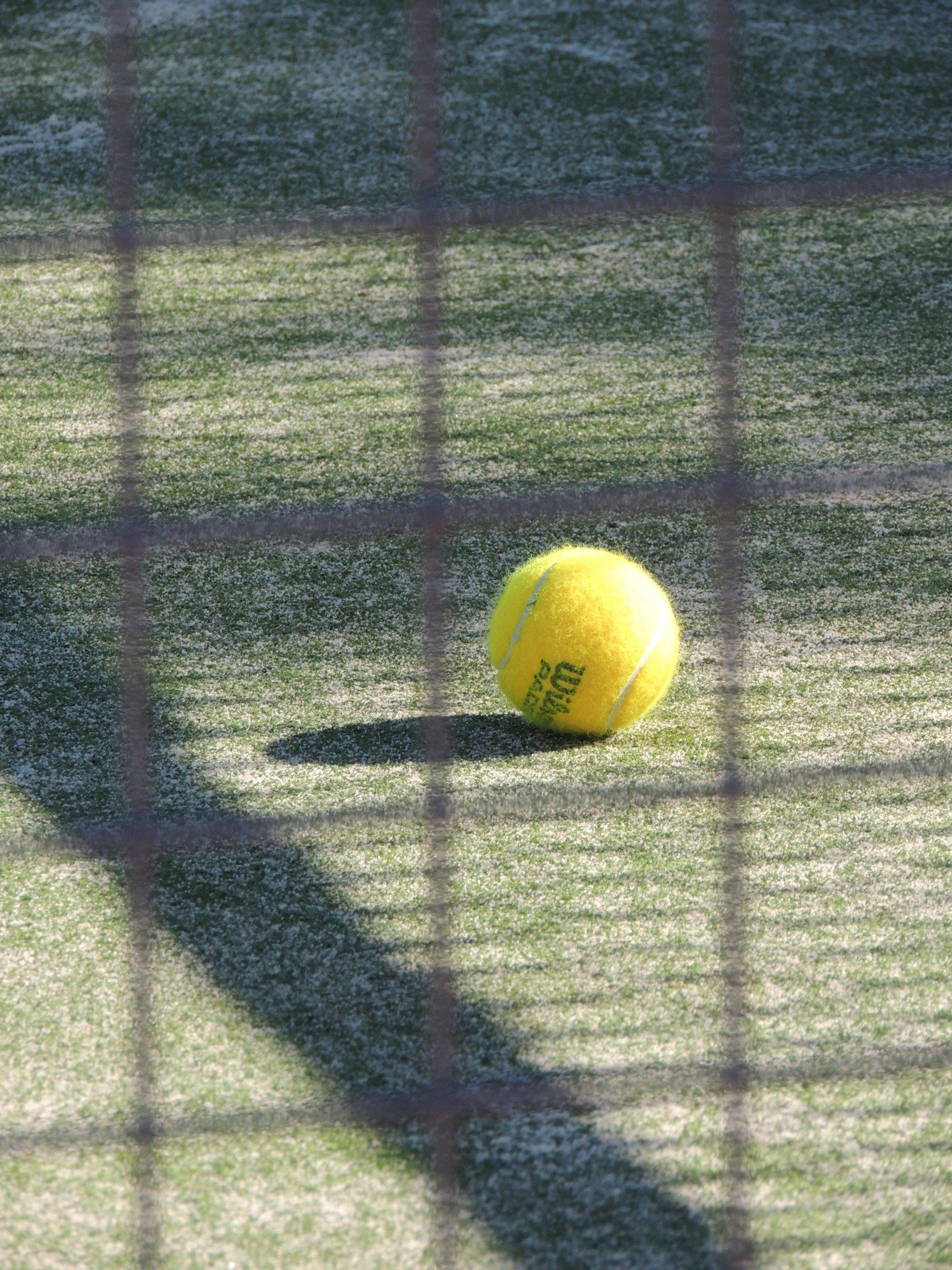 A tennis ball is sitting on a tennis court behind a net.