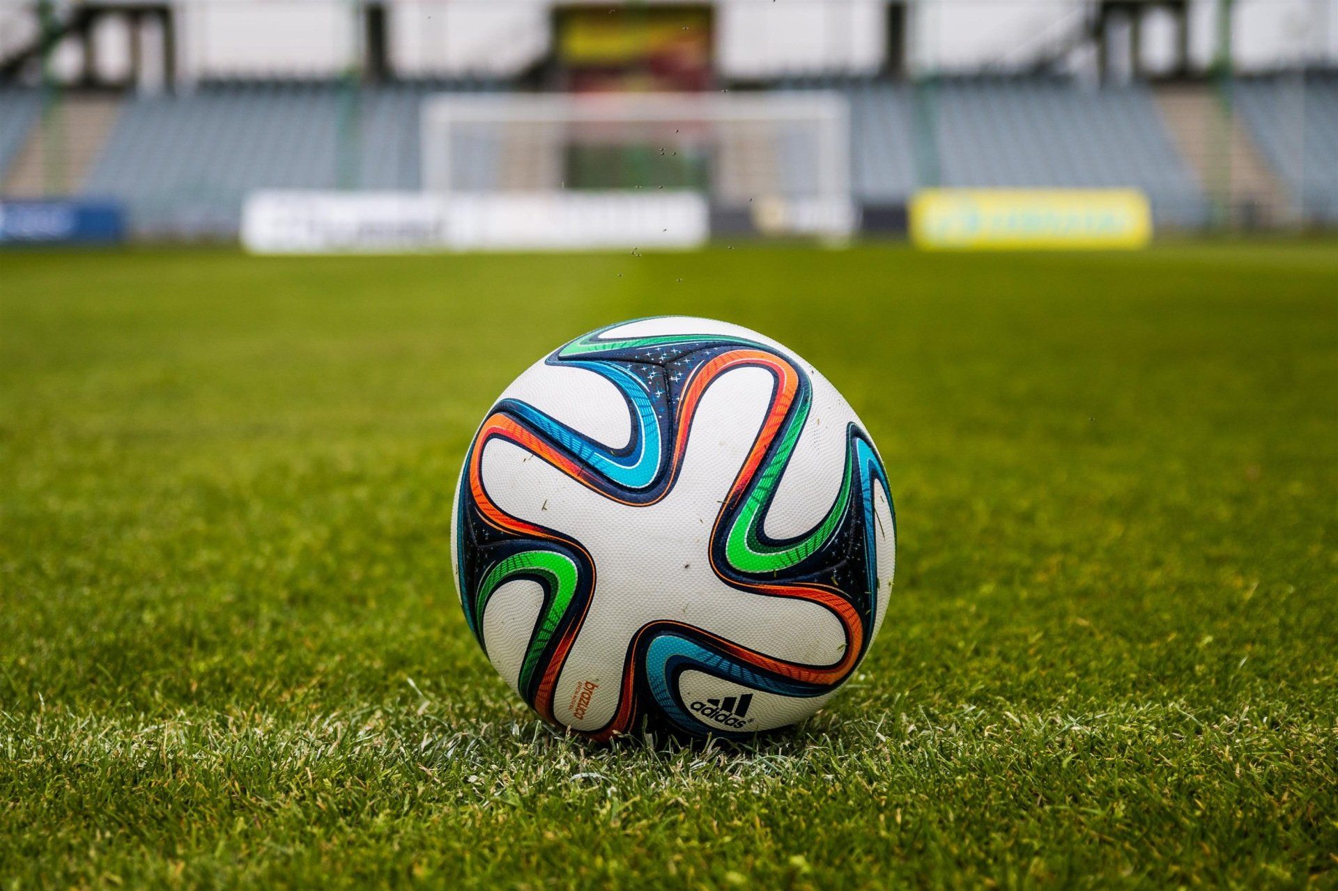 Ballon de football sur un terrain vert devant un but de football et des sièges de stade.