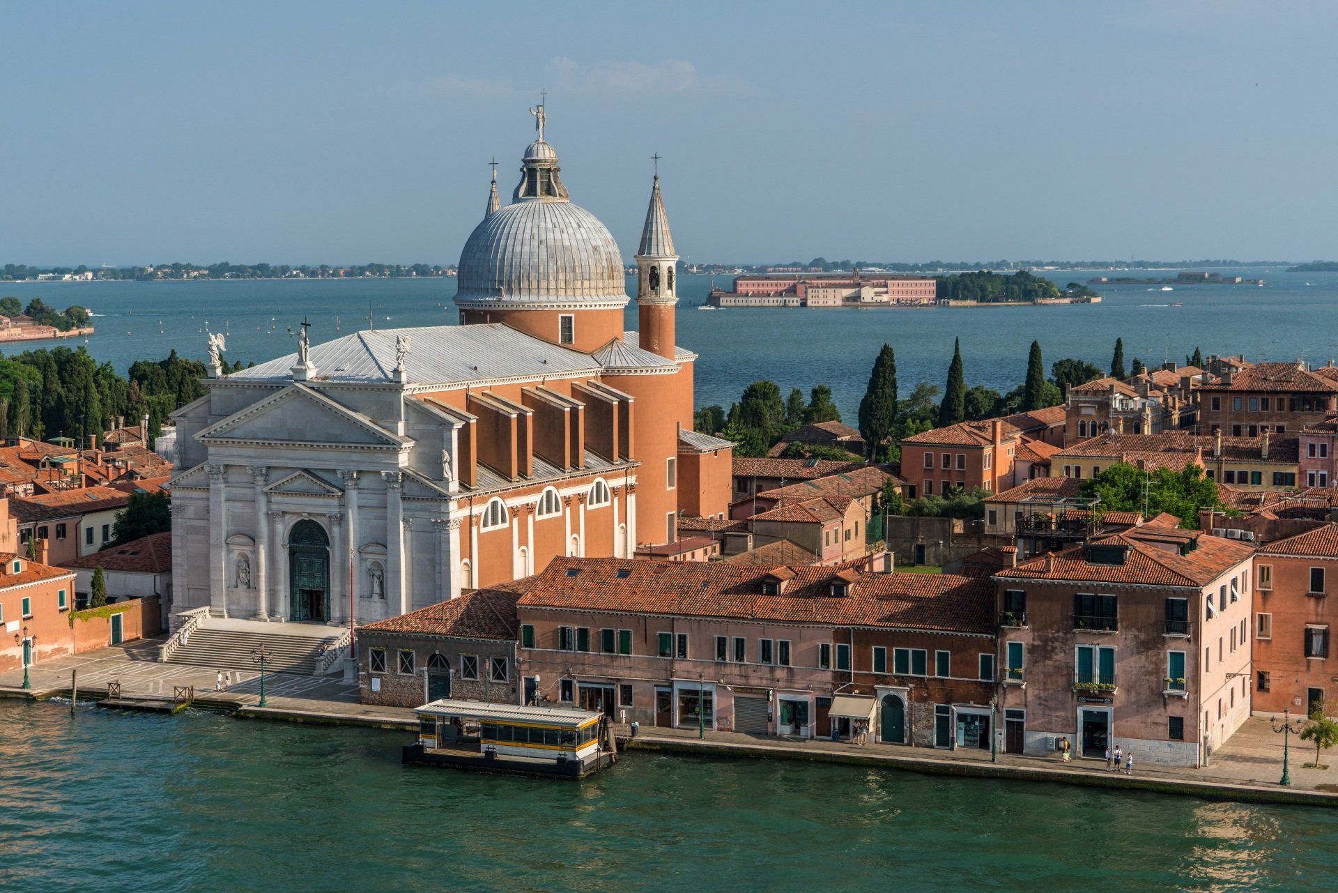 An aerial view of a city with a large church in the foreground and a body of water in the background.