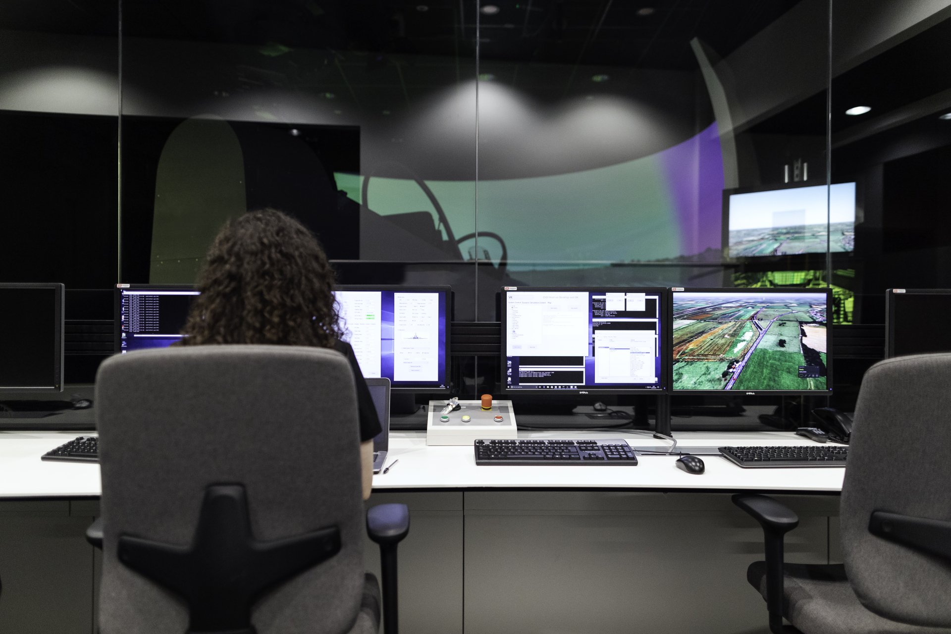 A woman sits at a desk in front of several computer monitors