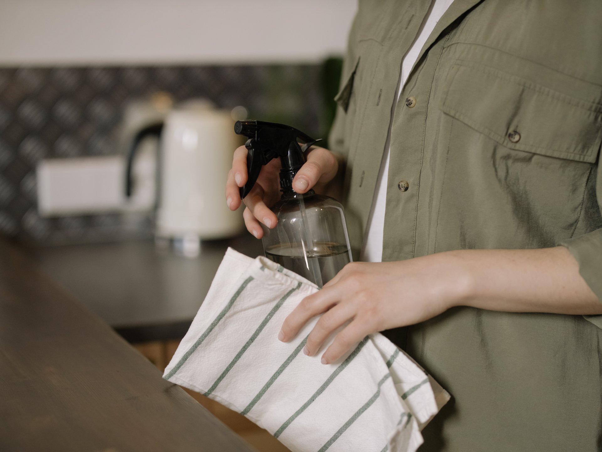 A woman is cleaning a counter with a spray bottle and a towel.