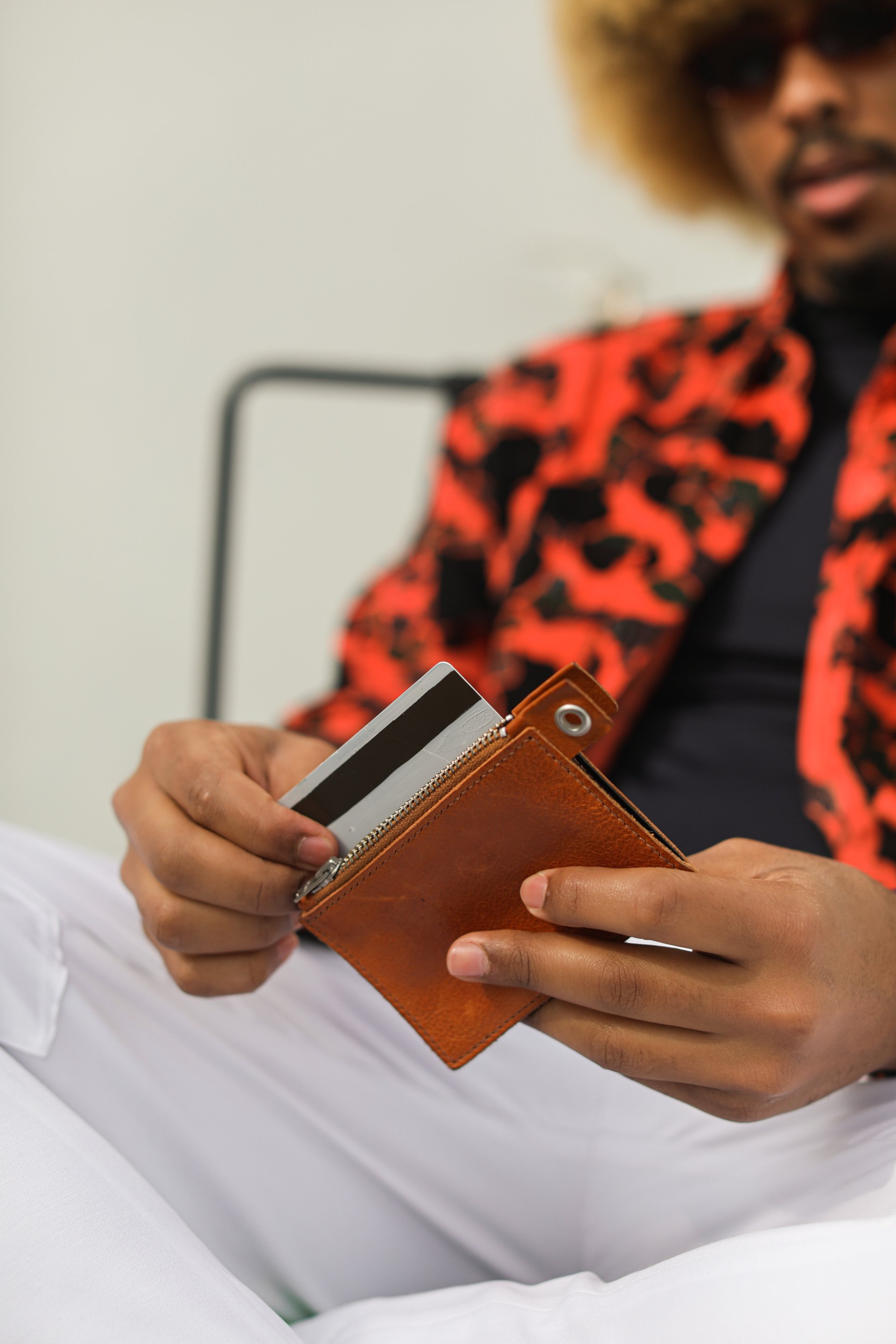 Person in red and black patterned jacket holding an open brown leather wallet, with a credit card partially visible.